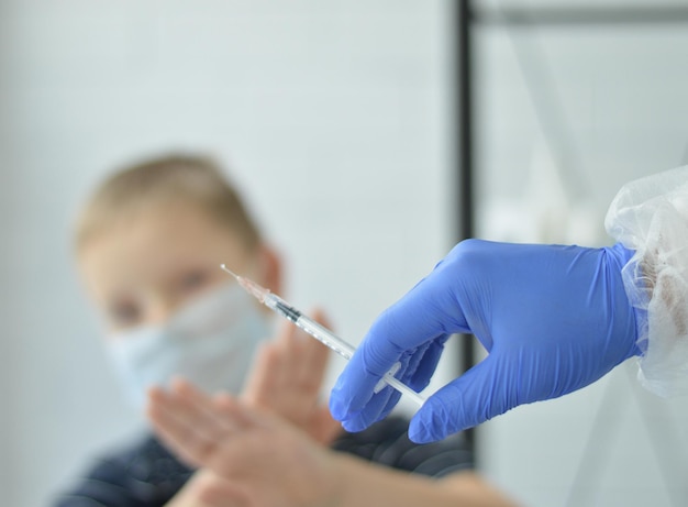 The concept of abandoning childhood vaccination a doctor in\
blue gloves preparing to enter a vaccine with a syringe into a boy\
children\'s vaccination