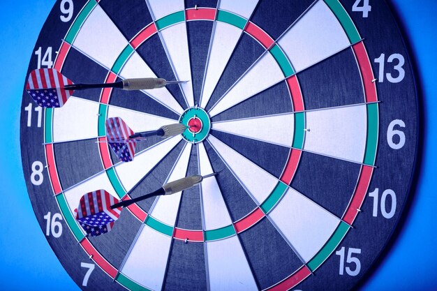 Concept achieving goal.Achieving goals in business, politics and life.Dartboard with darts painted with American flag stuck right into target.On blue background.