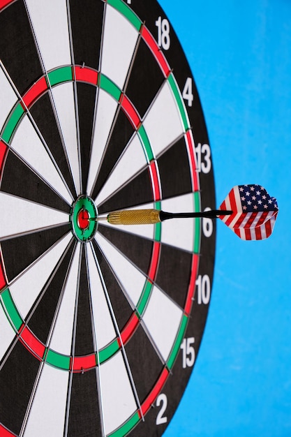 Concept achieving goal.Achieving goals in business, politics and life.Dartboard with darts painted with American flag stuck right into target.On blue background.