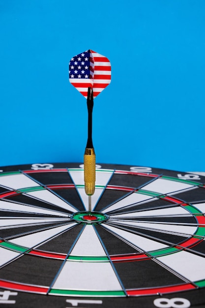 Concept achieving goal.Achieving goals in business, politics and life.Dartboard with darts painted with American flag stuck right into target.On blue background.