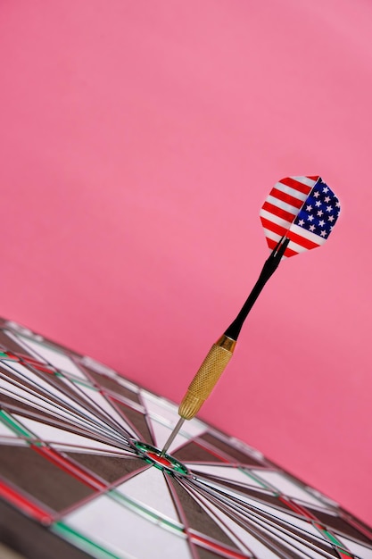 Photo concept achieving goal.achieving goals in business, politics and life.dartboard with darts painted with american flag stuck right into target.on pink background.