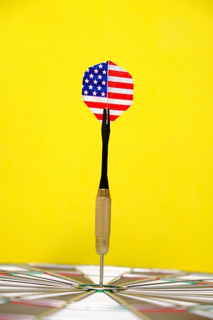 Концепция достижения цели. Достижение целей в бизнесе, политике и жизни. Дартборд с дротиками, окрашенными американским флагом, застрял прямо в мишени. На желтом фоне.