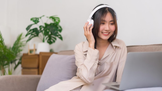 Concept of activity in living room asian woman is wearing\
headphone and watching movie on laptop