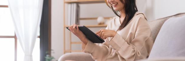 Concept of activity in living room Asian woman is wearing headphone and watching movie on tablet