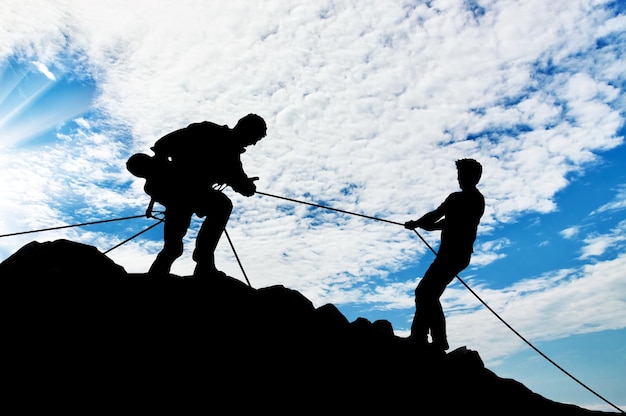 援助の概念。 2人の登山者のシルエットが助け合う