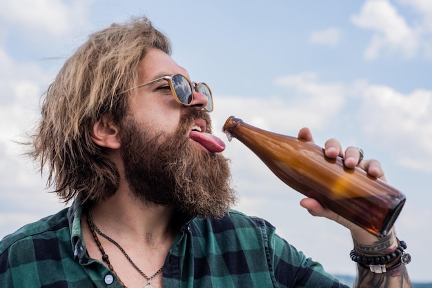 Photo concept of alcohol drinking man drink from glass bottle brutal man with water refresh with water bearded man wear checkered shirt casual male relax while drinking beer refreshing affect