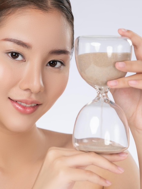 The concept of antiaging demonstrated by a closeup portrait of gorgeous young woman holding an hourglass Skincare treatment beauty care