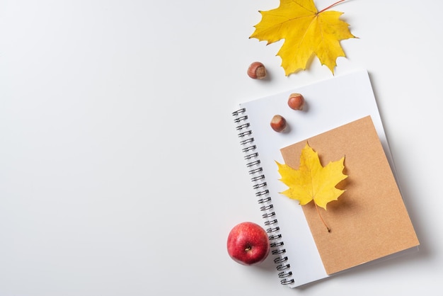 Concept autumn flat lay with yellow maple leaves on a notebook and notepad and a red apple on a white table Top view and copy space