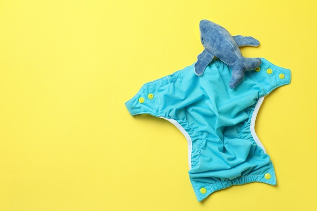 Concept of baby clothes with reusable diapers on yellow background