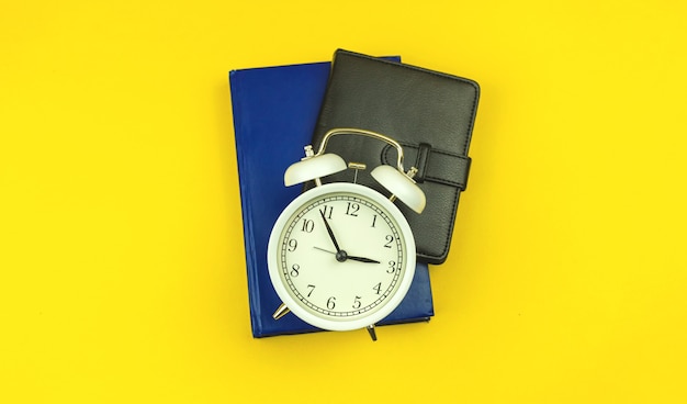 Concept of back to school, students education time background with alarm clock and diary notebooks on the yellow table, top view photo