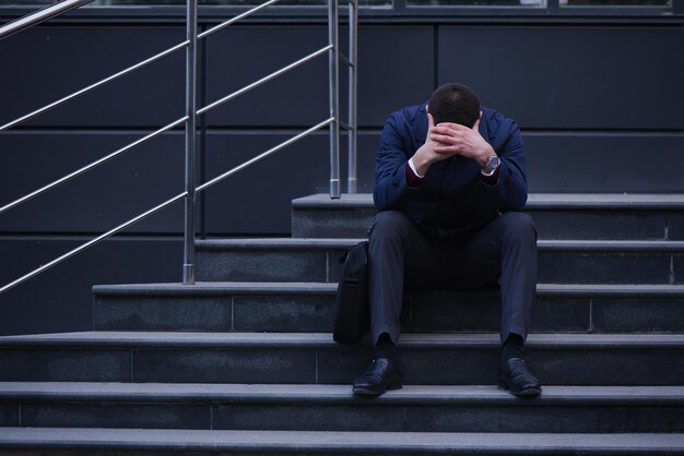 The concept of the bankruptcy of a business man sitting on stairs on the street holding his head