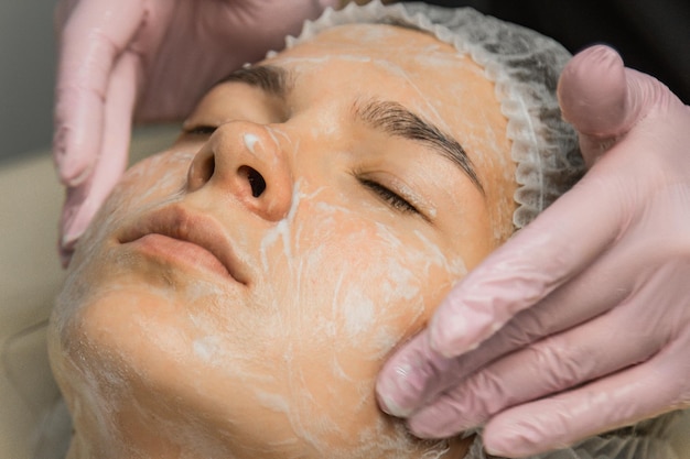 Concept beautician The hands of a cosmetologist put cream on the face of a woman Beautician applies a cream to the face of the girl