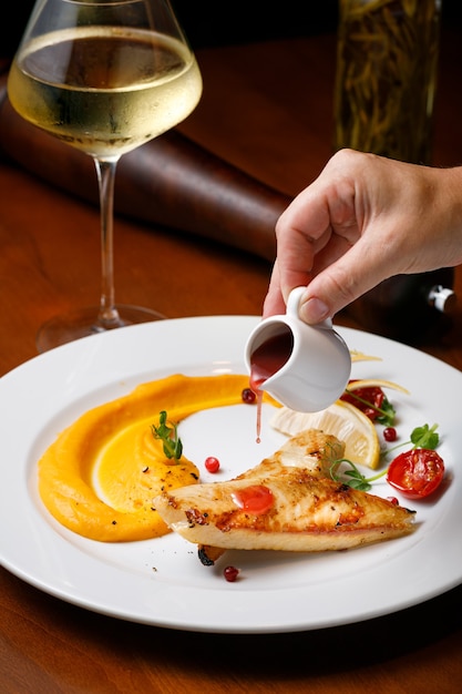 The concept of a beautiful european dish in the restaurant. Fried steak fillet fish with with berry sauce on a white plate with a glass of white wine. High quality photo.