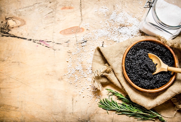 Il concetto di caviale nero caviale nero in una tazza con sale e rosmarino su un tavolo di legno