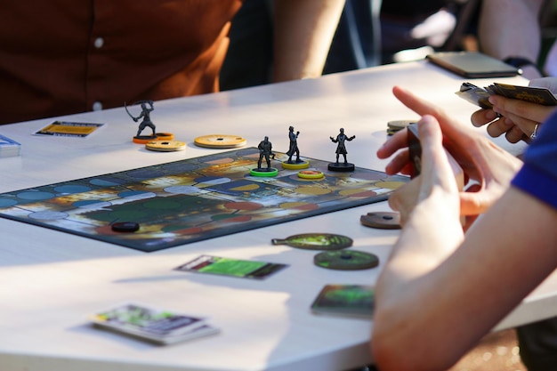 The concept of a board game and leisure Adults teenagers or children play board games Hands with playing cards chips and placed figures of characters on the table