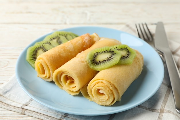 Concept of breakfast with plate of crepes rolls with kiwi slices on wooden table