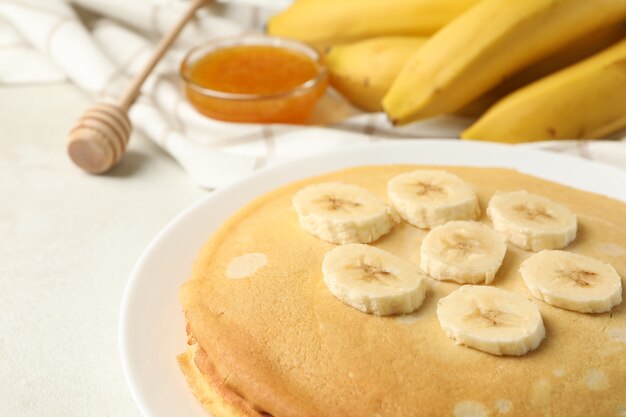 Concept of breakfast with plate of thin pancakes with banana, and jam on white textured background