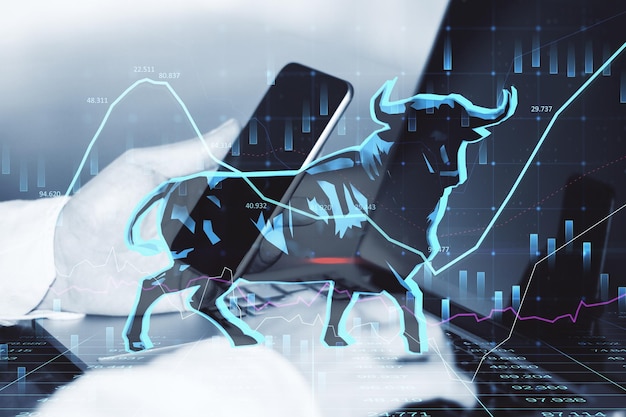 Concept of bullish market Close up of businessman hands using laptop and smartphone with glowing bull hologram over forex chart on blurry background Trade and invest concept Double exposure