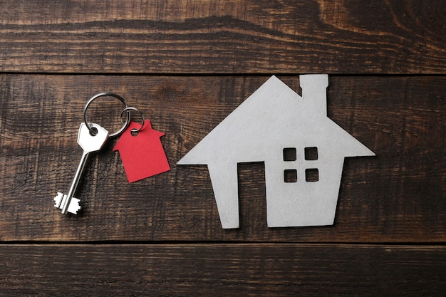 concept of buying a home. Decorative house with keys and keychain on a blue wooden table. top view