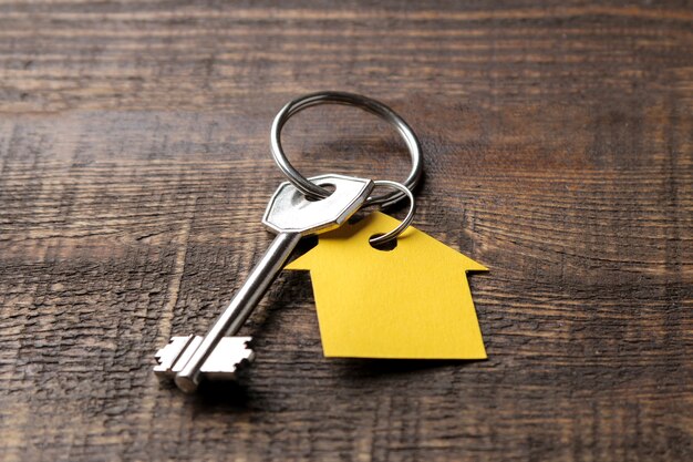 concept of buying a home. Keys with keychain house on a brown wooden background close-up.