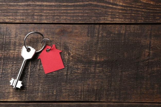 concept of buying a home. Keys with keychain house on a brown wooden background. view from above. with space for inscription