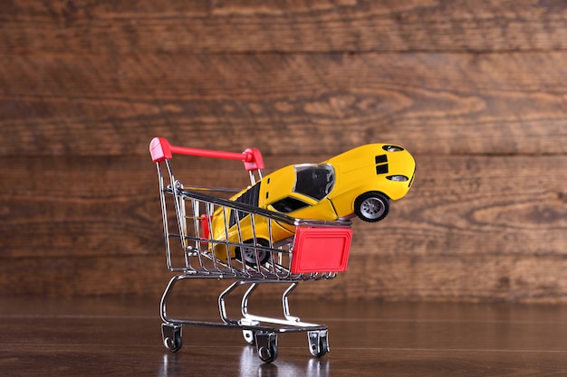 新しい車を購入する概念。木製のテーブルに買い物かごのおもちゃの車
