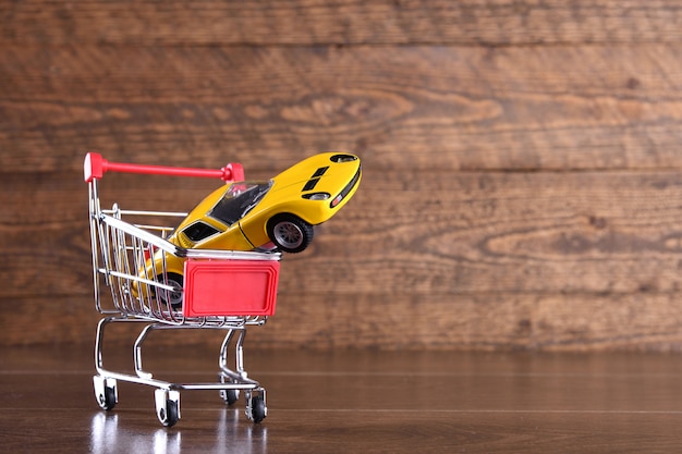 Concept of buying a new car. Toy car in shopping basket on wooden table