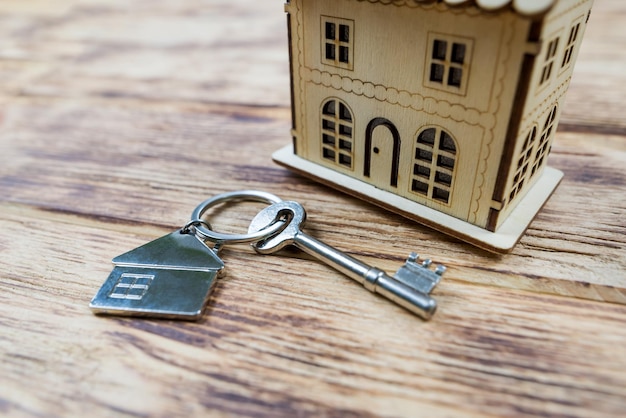 Foto il concetto di acquisto di una nuova casa o appartamento mutuo in affitto di prestito immobiliare primo piano di una casa di legno giocattolo con chiavi su uno sfondo di legno