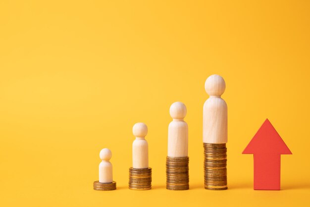 The concept of career growth and wealth increase Wooden figurines stand on a ladder made of coins on a yellow background red arrow pointing up