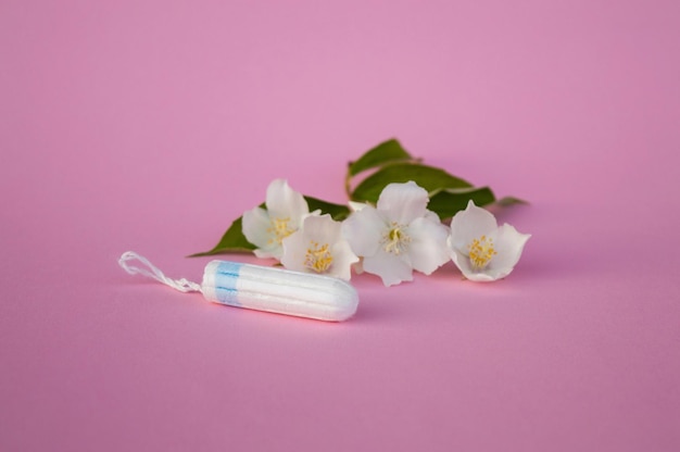 The concept of careful and gentle protection in critical days Menstruation period concept Hygienic white tampons for women with flowers jasmine on pink backround