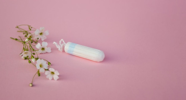 The concept of careful and gentle protection in critical days Menstruation period concept Hygienic white tampons for women with flowers on pink backround