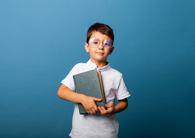 Concetto dell'infanzia, della scuola, dell'istruzione e della gente - ragazzo sorridente felice con i vetri che tengono un libro.