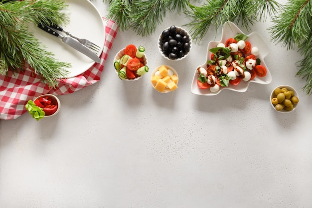 Concetto di cena di natale con insalata caprese e vari piatti di verdure per la festa di natale festiva sul tavolo bianco. vista dall'alto. spazio per il testo.