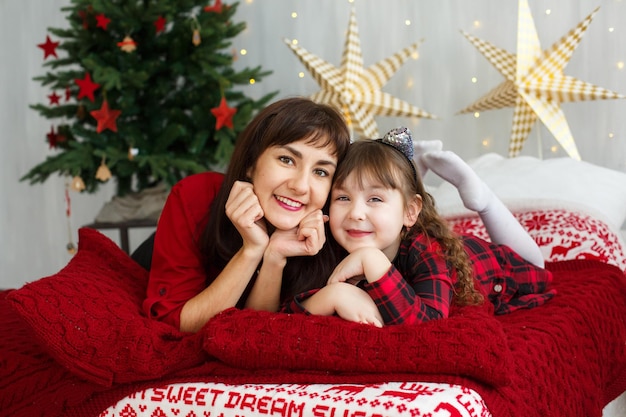 The concept of Christmas Happy mom and daughter child lying on bed by the Christmas tree