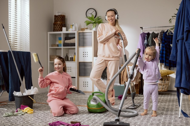 Concept of cleaning apartment on weekend mom and two daughters
clean up laundry room bathroom woman and little girls sweep vacuum
floor dance listen to music enjoy their time together