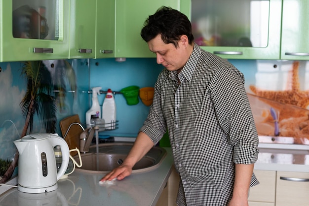 The concept of cleaning the kitchen a young man washes dishes and kitchen furniture a housewife a home chore