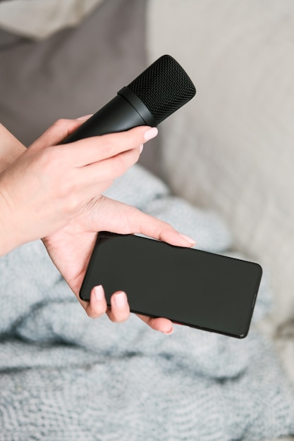 Concept for Clubhouse Drop-in audio is a voice-activated social media app. Smartphone and microphone in female hands on a light wall