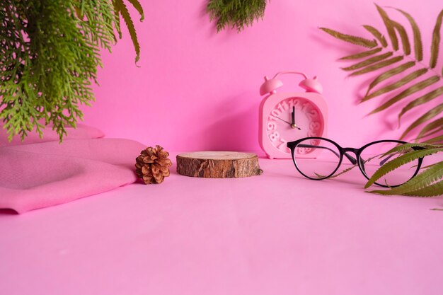 The concept of composition ideas featuring products. round wood on pink background decorated with glasses, clock, leaves and cloth