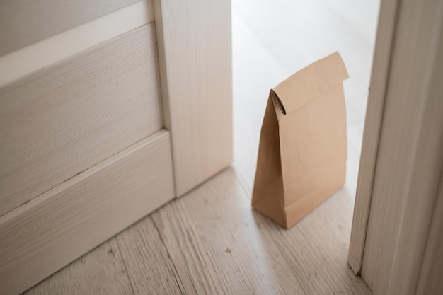 The concept of contactless delivery during the quarantine period Kraft paper bag with online purchase at the open entrance door in case of danger of the spread of coronavirus