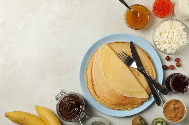 Concept of cooking breakfast with thin pancakes and ingredients on white textured background