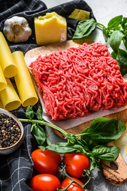 The concept of cooking cannelloni pasta with ground beef. ingredients Basil, cherry tomatoes, Parmesan, garlic. Gray background. top view