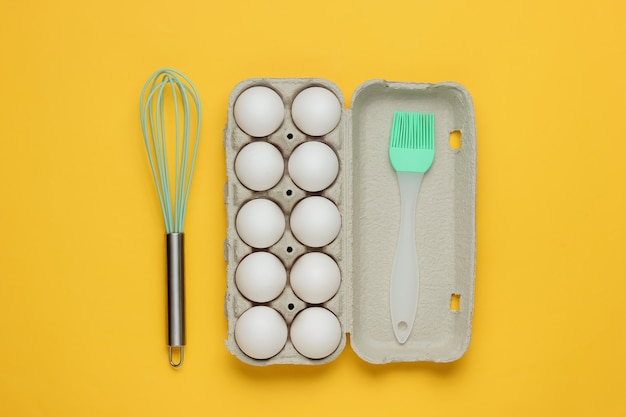 The concept of cooking cardboard tray of eggs kitchen tools whisk brush on yellow background