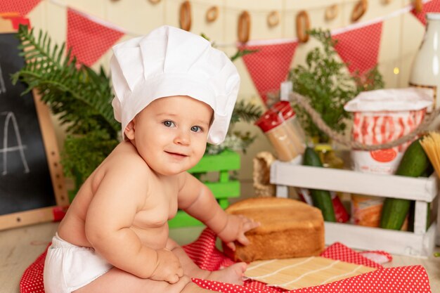 The concept of cooking, happy little child in a chef's hat sitting in the kitchen with bread