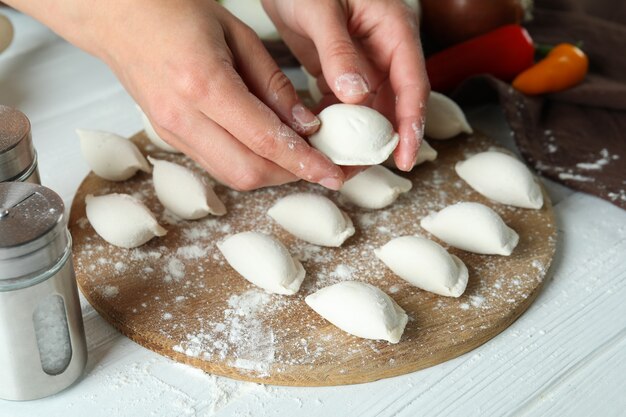 Concetto di cucinare vareniki o pierogi su un tavolo di legno bianco