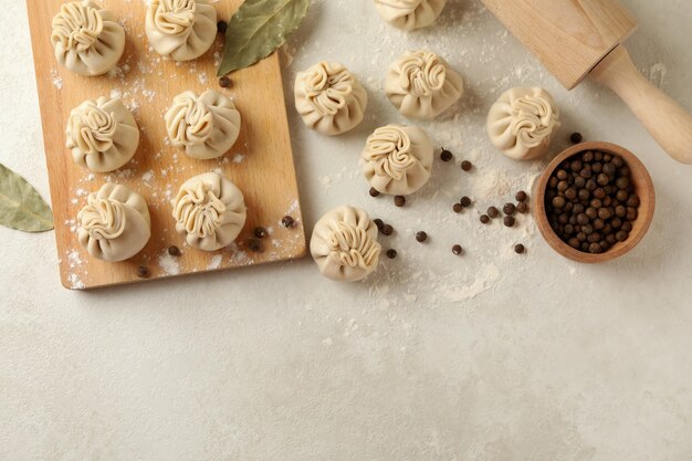 Concept of cooking with raw khinkali and spices on white textured table