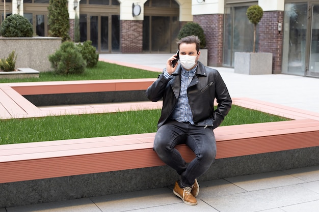 Concept of coronavirus quarantine, man with medical face mask using the phone to search for news. Air pollution