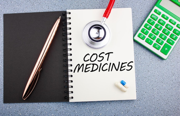 The concept of the cost of medicinesThe inscription COST OF MEDICINE on a notebook next to medicines and a stethoscope Cost and costs of treatment