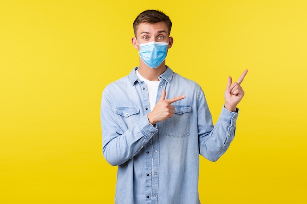 Concept of covid-19 pandemic outbreak, lifestyle during coronavirus social distancing. Surprised guy in medical mask and casual clothes asking question about product, pointing upper right corner.