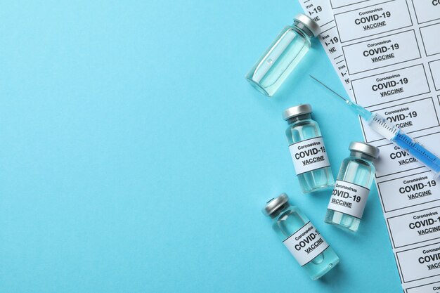 Концепция вакцинации Covid - 19 с флаконами и шприцем на синем фоне