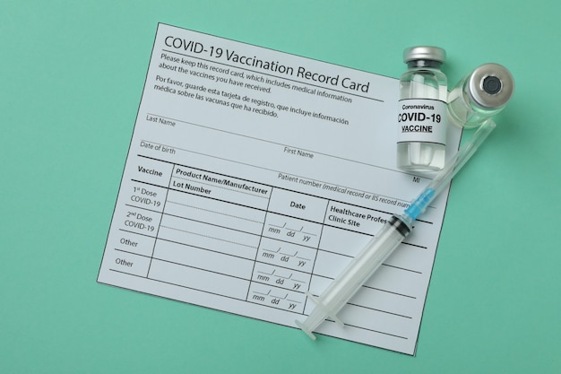 Photo concept of covid - 19 vaccination with vials of vaccine on mint